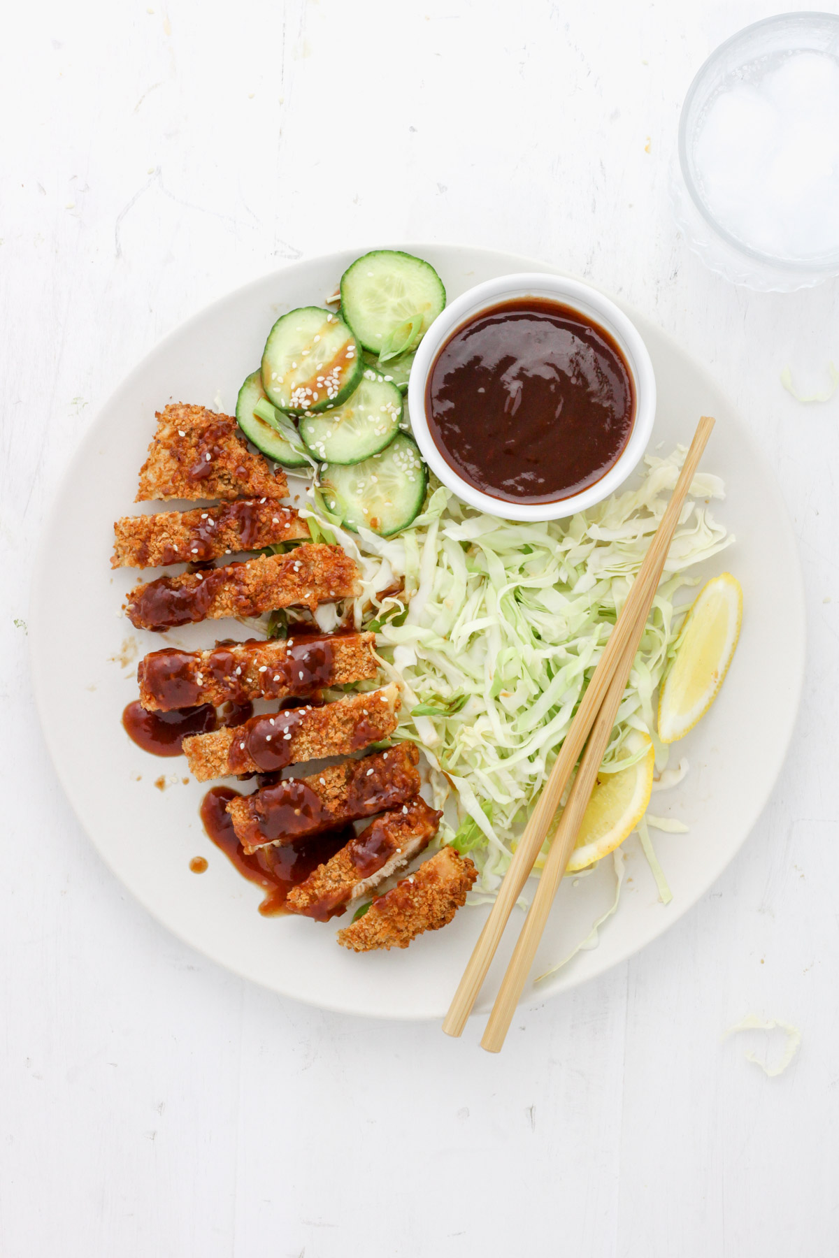 A white plate with air fryer chicken katsu topped with tonkatsu sauce, green cabbage and cucumbers.